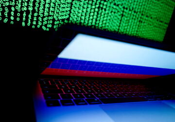 A Russian flag is seen on the laptop screen in front of a computer screen on which cyber code is displayed, in this illustration picture taken March 2, 2018